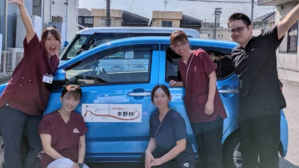 社用車の前に集まった訪問看護ステーション木野村のスタッフ5名。車体には木野村のロゴと犬のイラストが入っている。
